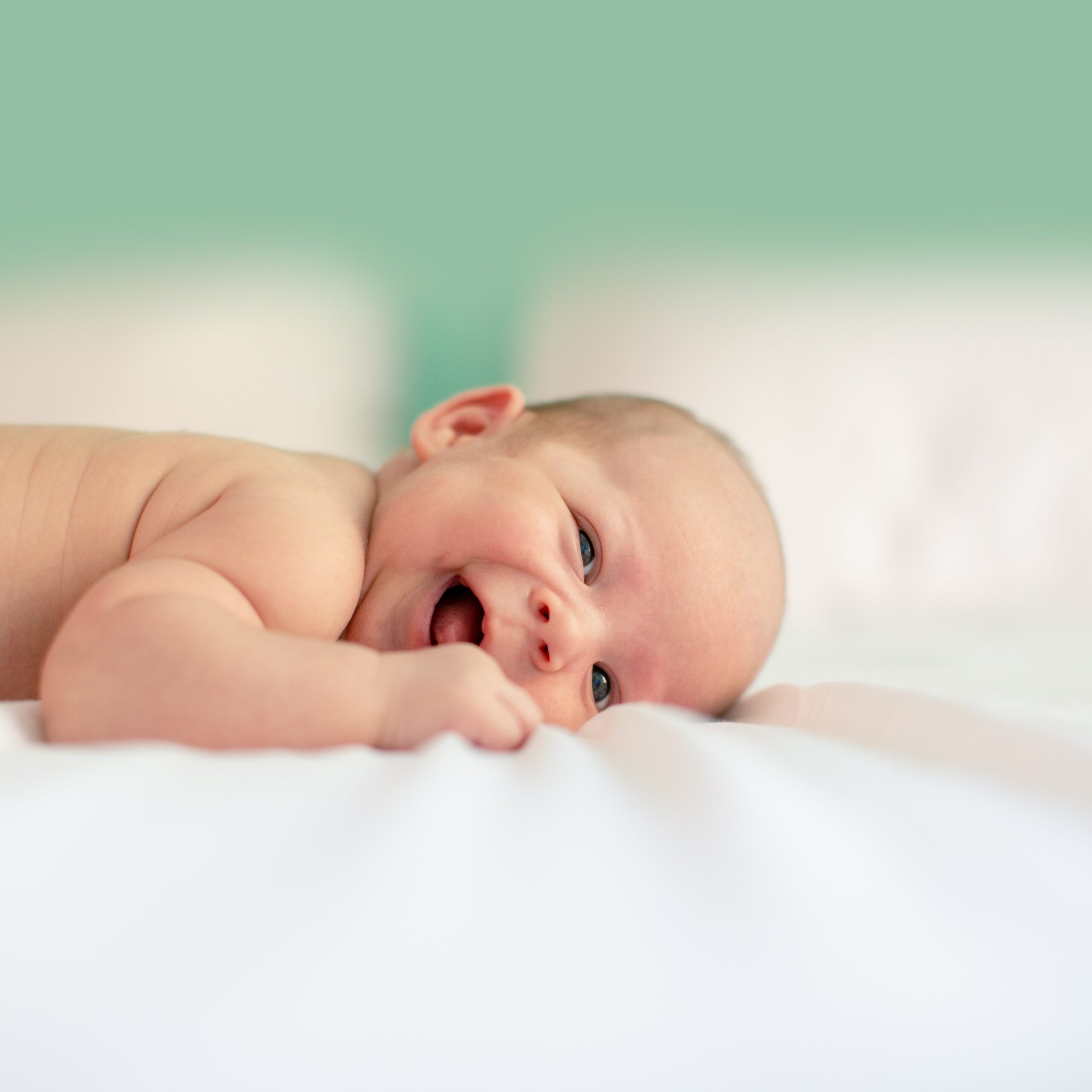 Vaasan Setlementin palvelut lapsille ja perheille. Pieni vauva makaa vatsallaan valkoisella alustalla ja nauraa. Setlementin Esikot-ryhmä on tarkoitettu perhettä suunnitteleville, vauvaa odottaville tai ensimmäisen vauvan jo saaneille.